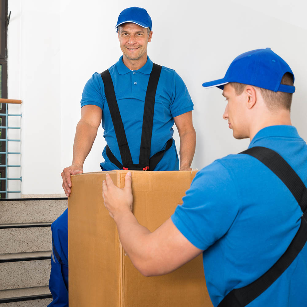 Kraftmann Umzüge - Möbelpacker beim Transport von schweren Umzugskarton durch Treppenhaus